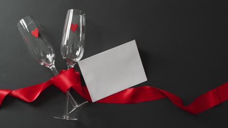 Champagne-glasses-with-hearts,-red-ribbon-and-white-card-with-copy-space-at-valentine's-day