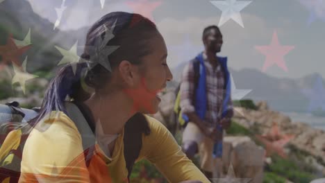 Animation-of-american-flag-over-smiling-diverse-couple-sitting-in-mountains