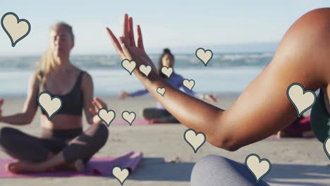 Animation-of-yellow-hearts-over-women-practicing-yoga-on-beach