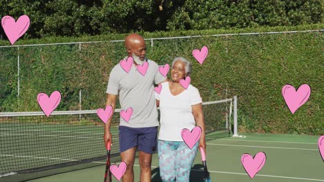 Animation-of-pink-hearts-over-smiling-senior-african-american-couple-embracing-outdoors-after-tennis
