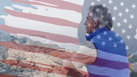 Animation-of-american-flag-over-senior-caucasian-man-sitting-on-rocks-in-mountains