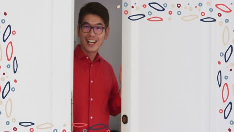 Animation-of-colourful-patterned-frame-over-smiling-asian-man-in-glasses-welcoming-at-front-door