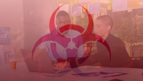 Animation-of-biohazard-symbol-over-diverse-business-people-using-laptop-in-office