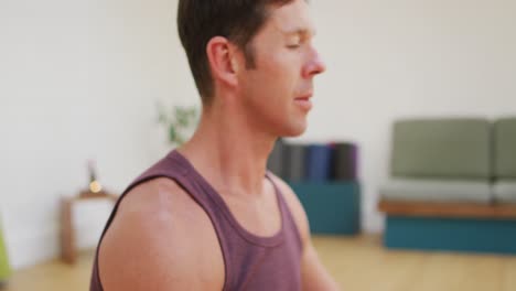Portrait-of-smiling-caucasian-man-practicing-yoga-sitting-in-lotus-position-at-yoga-studio