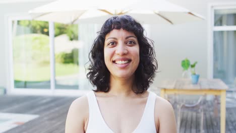 Portrait-of-laughing-biracial-woman-outside-on-terrace-of-modern-house-in-the-sun