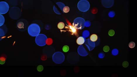Animation-of-glowing-sparkler-and-colourful-christmas-bokeh-light-spots-on-black-background