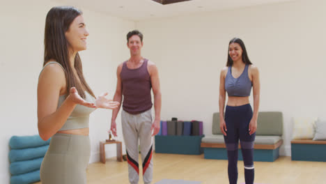 Smiling-caucasian-female-instructor-talking-to-happy-diverse-man-and-woman-during-yoga-class