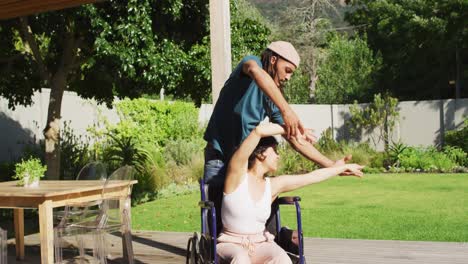 Happy-biracial-couple-dancing-on-terrace-in-garden,-woman-in-wheelchair,-man-with-dreadlocks