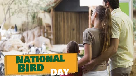Animation-of-national-bird-day-text-in-green-over-parents-and-daughter-watching-penguins-at-zoo
