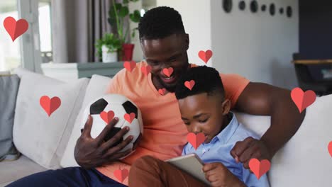 Animation-Roter-Herzen-über-Einem-Glücklichen-Afroamerikanischen-Vater-Und-Sohn,-Die-Zu-Hause-Auf-Der-Couch-Ihr-Smartphone-Benutzen