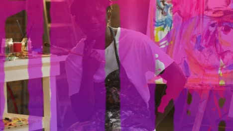 Animation-of-pink-paint-dripping-over-smiling-african-american-male-artist-sitting-in-studio