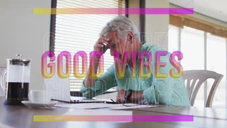 Animation-of-good-vibes-in-pink-over-happy-caucasian-senior-man-using-laptop-in-kitchen