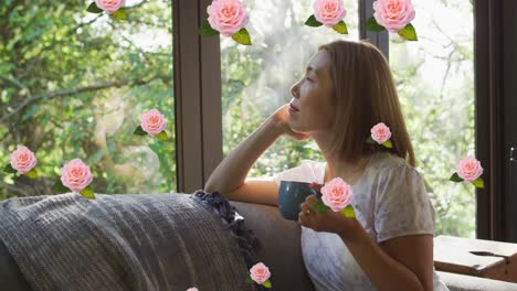 Animation-of-pink-roses-over-smiling-asian-women-drinking-coffee-looking-out-of-window-at-home