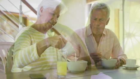 Animation-of-orange-slices-over-happy-caucasian-senior-couple-having-breakfast-at-home