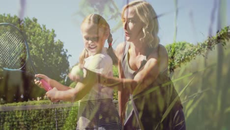 Animation-of-grass-over-caucasian-mother-and-daughter-playing-tennis-outdoors