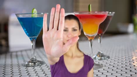 Animation-of-caucasian-woman-making-stop-hand-sign,-over-cocktail-glasses-on-bar