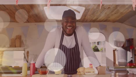 Animation-of-spots-of-light-floating-over-smiling-african-american-fast-food-seller