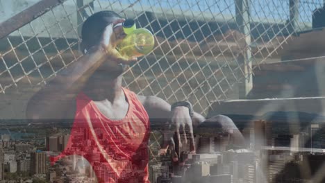 Animation-of-cityscape-over-african-american-male-athlete-drinking-water-during-exercise