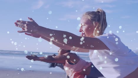 Animation-Von-Lichtpunkten-über-Verschiedenen-Freundinnen,-Die-Am-Strand-Yoga-Praktizieren