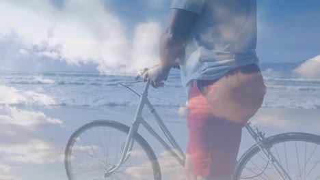 Animation-of-senior-african-american-man-walking-with-bicycle-at-beach-over-clouds
