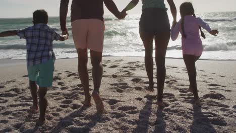 Back-view-of-hispanic-mother,-father,-son-and-daughter-holding-hands-and-walking-on-beach