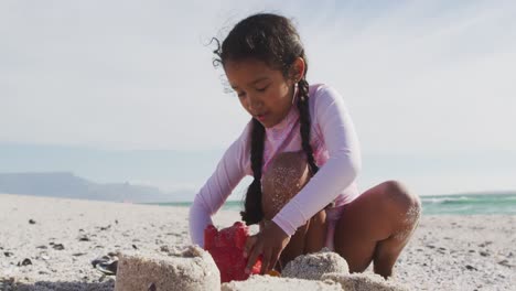 Glückliches-Hispanisches-Mädchen,-Das-Am-Strand-Sitzt-Und-Eine-Sandburg-Baut