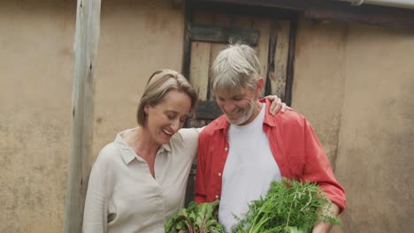 Lächelndes-älteres-Kaukasisches-Paar,-Das-Einen-Korb-Mit-Gemüse-Umarmt-Und-In-Der-Hand-Hält