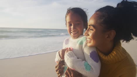 Portrait-of-happy-hispanic-mother-and-daughter-embracing-on-beach-at-sunset