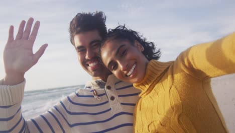 Portrait-of-happy-hispanic-couple-standing-on-beach,-taking-selfie