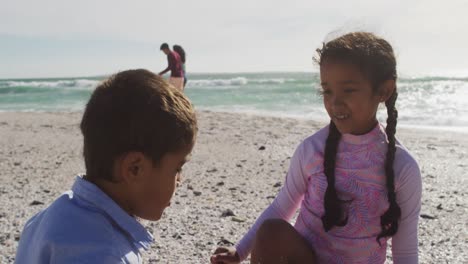 Happy-hispanic-brother-and-sister-playing-on-beach-with-sand