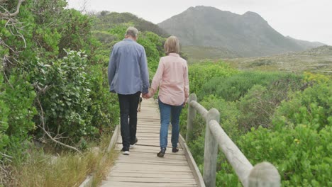 Smiling-senior-caucasian-couple-holding-hands-and-walking-on-path