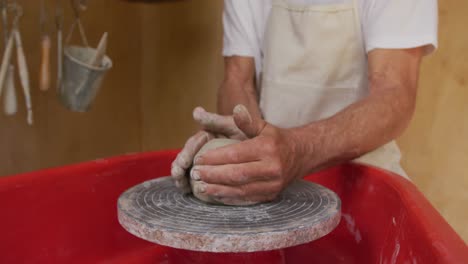 Senior-caucasian-man-wearing-apron-making-pottery-in-his-workshop