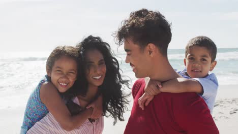 Porträt-Glücklicher-Hispanischer-Eltern,-Die-Ihre-Kinder-Huckepack-Am-Strand-Tragen