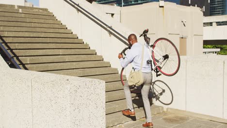 Back-view-of-african-american-man-carrying-bike-upstairs-in-city