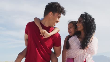 Happy-hispanic-parents-carrying-children-on-piggyback-and-walking-on-beach
