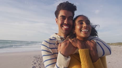 Porträt-Eines-Glücklichen-Hispanischen-Paares,-Das-Am-Strand-Steht-Und-Sich-Umarmt