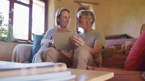 Lächelndes-älteres-Kaukasisches-Paar,-Das-Ein-Tablet-Benutzt-Und-Im-Wohnzimmer-Sitzt