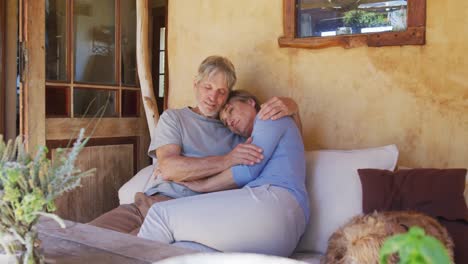 Smiling-senior-caucasian-couple-embracing-and-relaxing-on-porch-with-pet-dog
