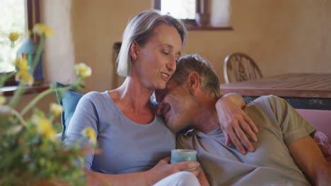 Smiling-senior-caucasian-couple-embracing-and-drinking-coffee-in-living-room