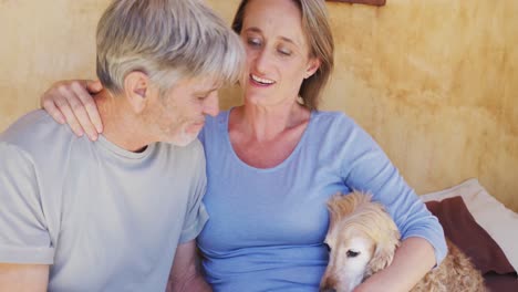 Smiling-senior-caucasian-couple-embracing-and-relaxing-on-porch-with-pet-dog