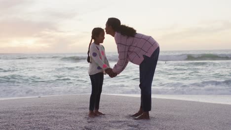 Happy-hispanic-mother-kissing-daughter-on-beach-at-sunset