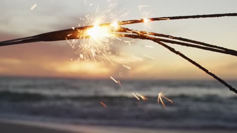 Lit-sparklers-glowing,-with-sea-and-sunset-in-background