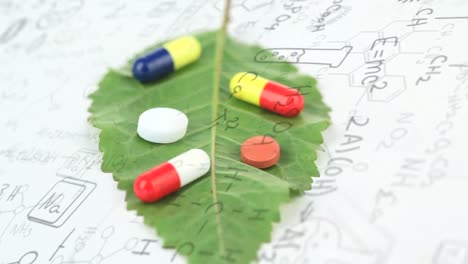 Animation-of-pills-on-leaf-over-chemical-formulas-on-white-background