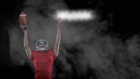 Male-rugby-player-holding-a-ball-pointing-over-stadium-lights-against-smoke-on-black-background