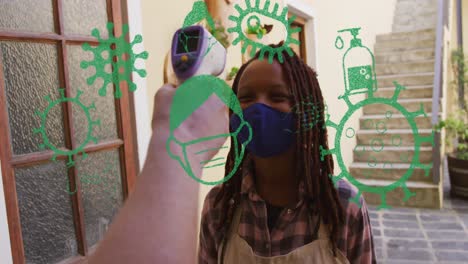 Animation-Von-Virussymbolen-über-Einer-Afroamerikanischen-Frau-Mit-Gesichtsmaske,-Die-Die-Temperatur-Misst