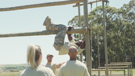 Diverse-group-watching-fit-african-american-male-soldier-with-deadlocks-climbing-on-obstacle-course