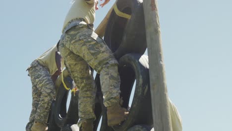 Eine-Vielfältige-Gruppe-Männlicher-Soldaten-In-Kampfuniform-Klettert-Auf-Einem-Armee-Hindernisparcours-In-Der-Sonne-Auf-Die-Reifenwand