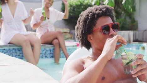 Happy-african-american-man-wearing-sunglasses-drinking-in-pool-with-friends-at-pool-party