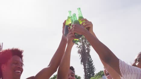 Happy-diverse-friends-making-toast-with-bottles-of-beer-in-the-sun-at-outdoor-party