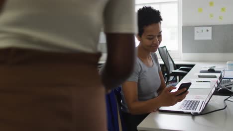 Glückliche-Afroamerikanische-Frau,-Die-Im-Büro-Ihr-Smartphone-Benutzt-Und-Ihren-Geschäftskollegen-Begrüßt